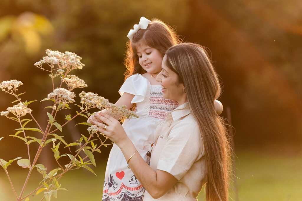 A joyful mother and daughter observe flowers in a sunlit garden, creating a warm family moment.