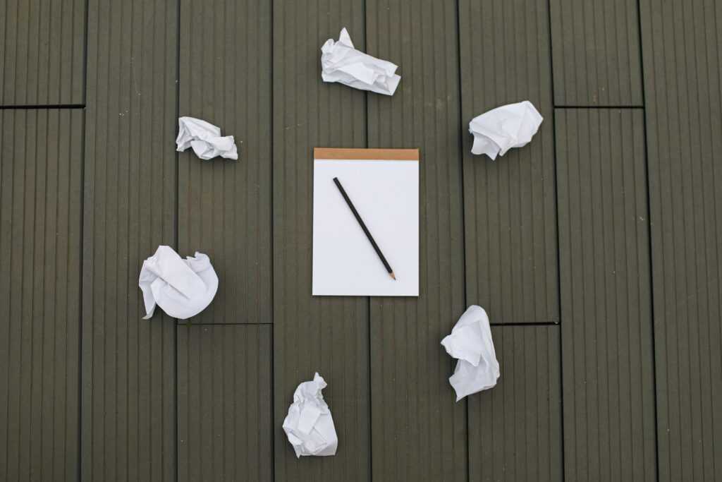 A blank pad and pencil surrounded by crumpled paper on a wooden surface, symbolizing a creative brainstorming process.