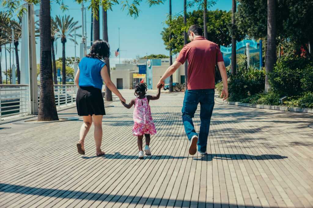 A family enjoys a walk together on a sunny day, holding hands and smiling.