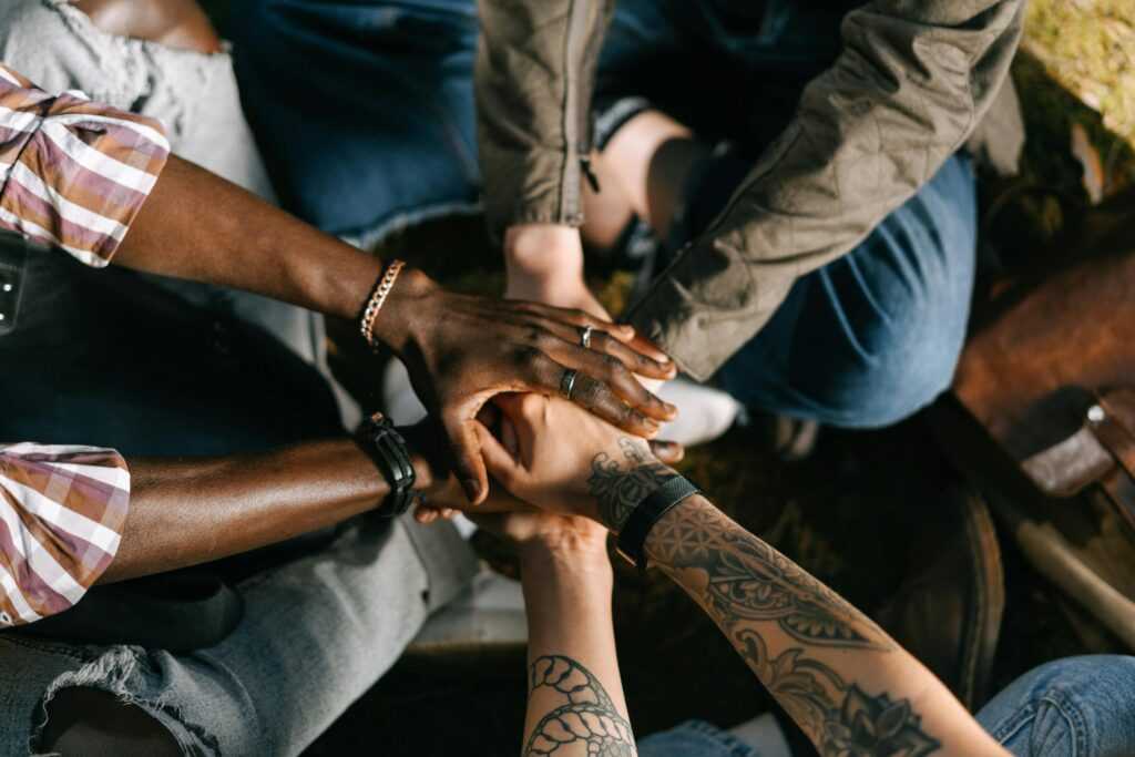 A diverse group of individuals uniting in solidarity with hands stacked together outdoors.