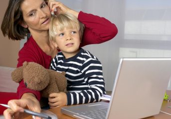 A mother multitasks by talking on the phone while managing work and child at home.