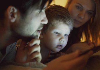 A family of three gathered closely, illuminated by the glow of a digital tablet.