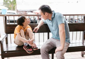A heartfelt interaction between father and son sitting on a wooden bench outdoors, promoting bonds and autism awareness.