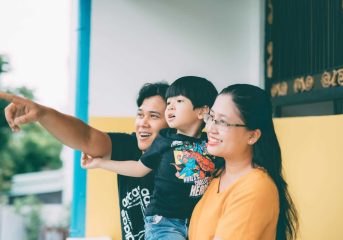 Asian family enjoying togetherness outdoors, pointing at something with smiles.